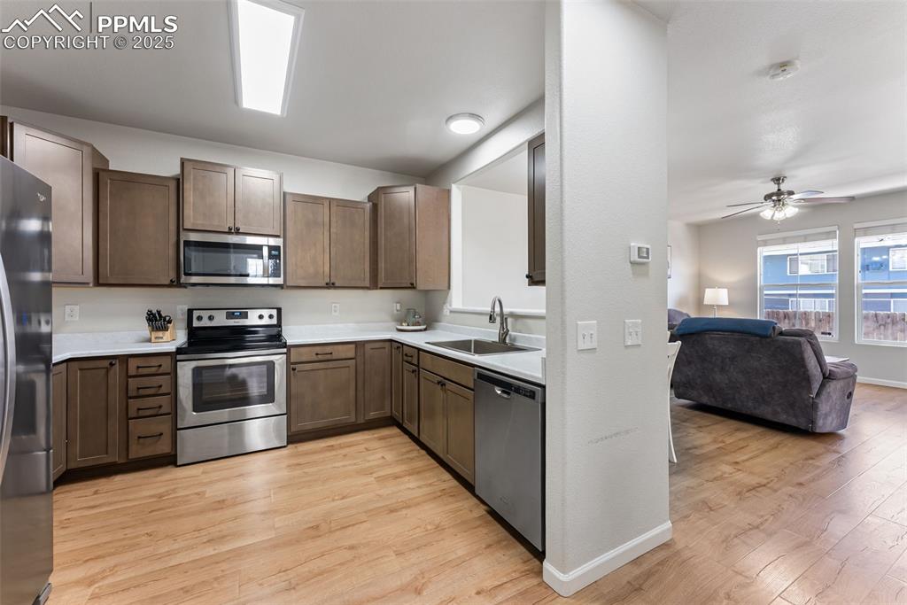 Kitchen with appliances with stainless steel finishes, light wood-style flooring, open floor plan, dark brown cabinetry, and a ceiling fan