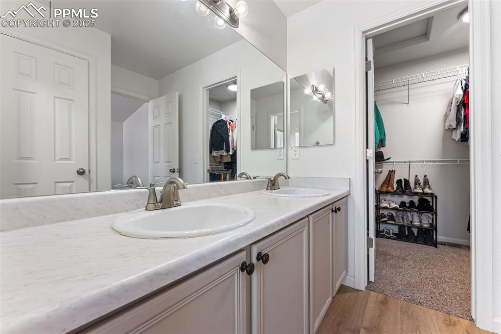 Bathroom with a spacious closet, light wood-style flooring, and double vanity