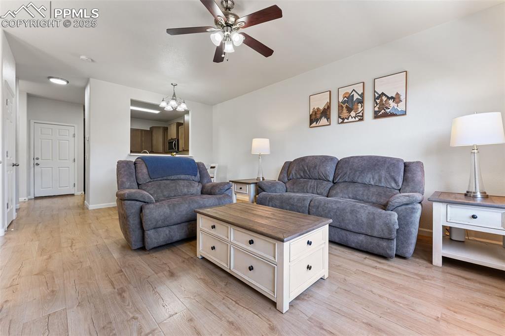 Living area with a chandelier, light wood-style floors, and ceiling fan