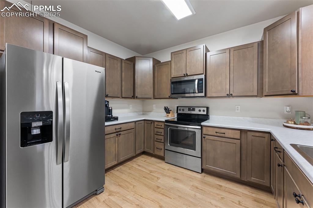 Kitchen featuring stainless steel appliances, light wood-type flooring, and light stone countertops