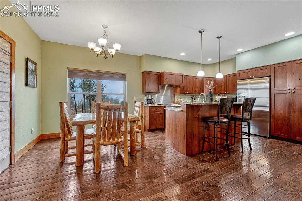 Kitchen featuring stainless steel refrigerator with ice dispenser, a chandelier, dark wood finished floors, a breakfast bar, and a sink