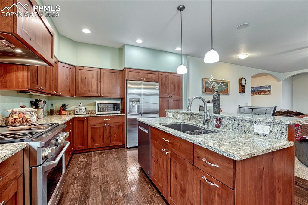 Kitchen featuring stainless steel appliances, a sink, dark wood-style flooring, and brown cabinetry