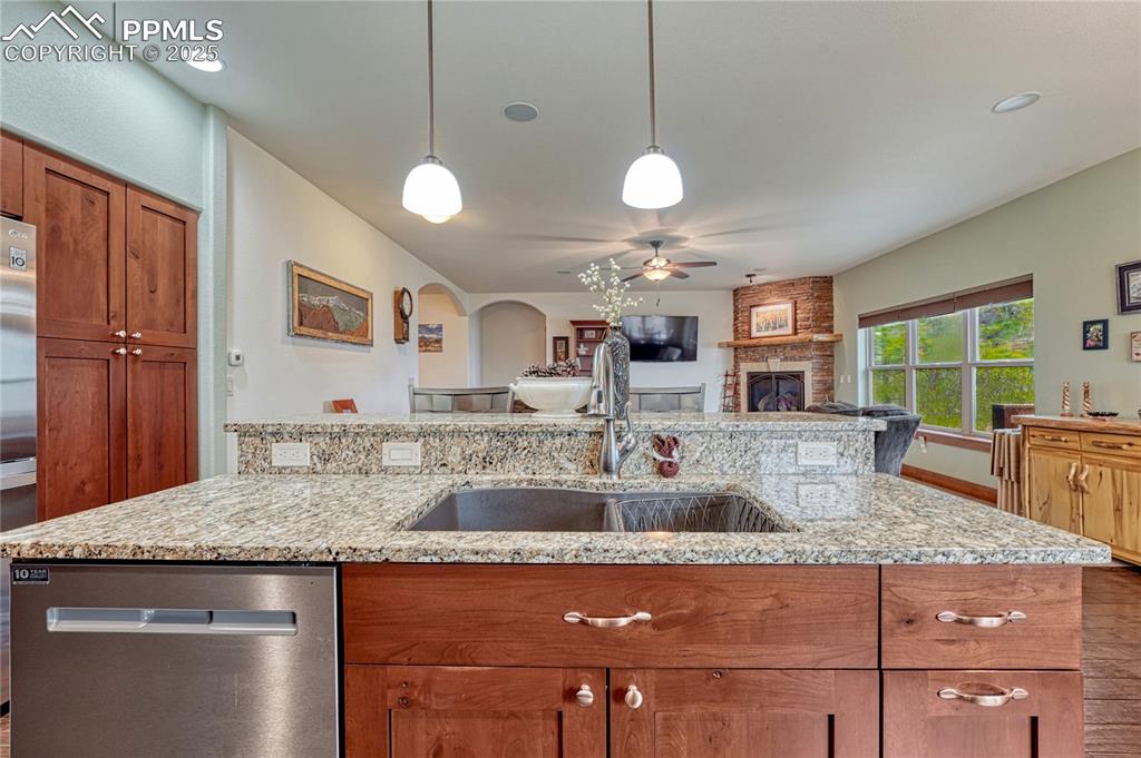 Kitchen with appliances with stainless steel finishes, a ceiling fan, brown cabinetry, a stone fireplace, and a sink