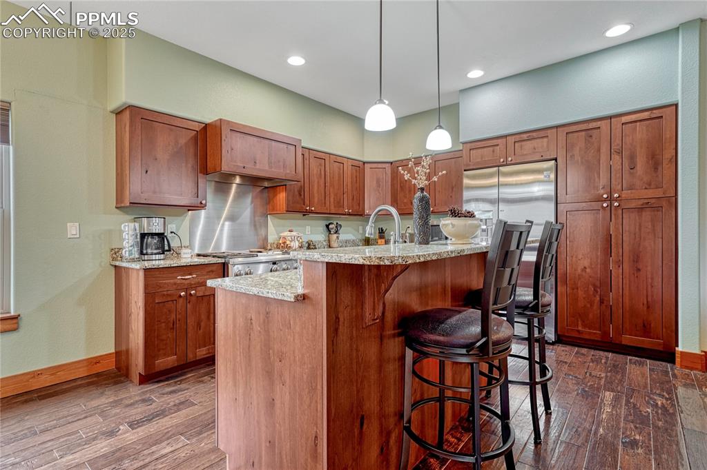 Kitchen with dark wood finished floors, a kitchen bar, light stone counters, hanging light fixtures, and recessed lighting