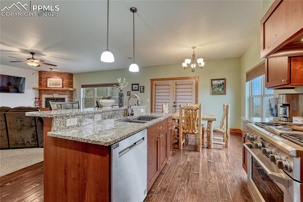 Kitchen with appliances with stainless steel finishes, a sink, ceiling fan, dark wood-style flooring, and a fireplace