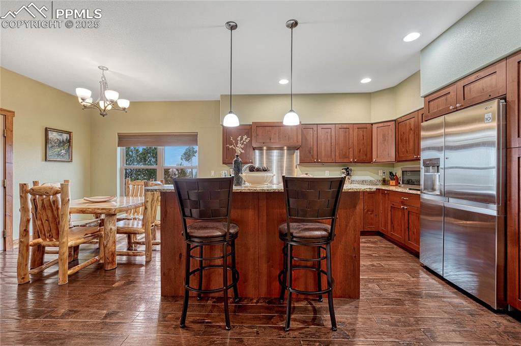 Kitchen with appliances with stainless steel finishes, dark wood finished floors, brown cabinetry, a breakfast bar, and recessed lighting