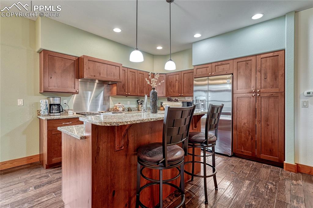 Kitchen featuring stainless steel fridge with ice dispenser, dark wood-type flooring, baseboards, a kitchen breakfast bar, and hanging light fixtures