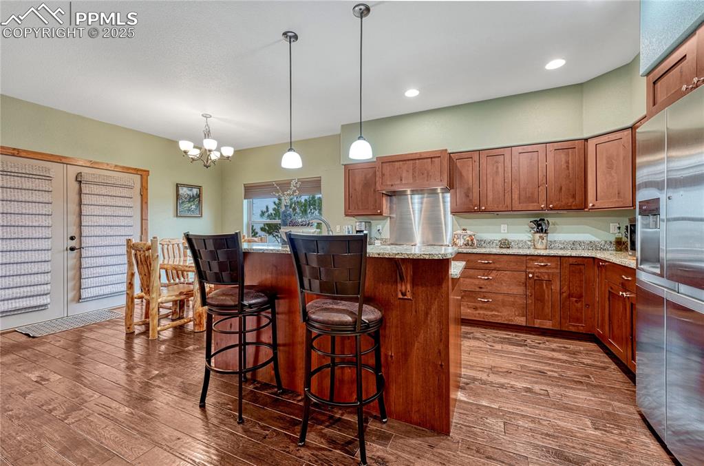 Kitchen with stainless steel refrigerator with ice dispenser, a chandelier, dark wood finished floors, brown cabinetry, and a breakfast bar area