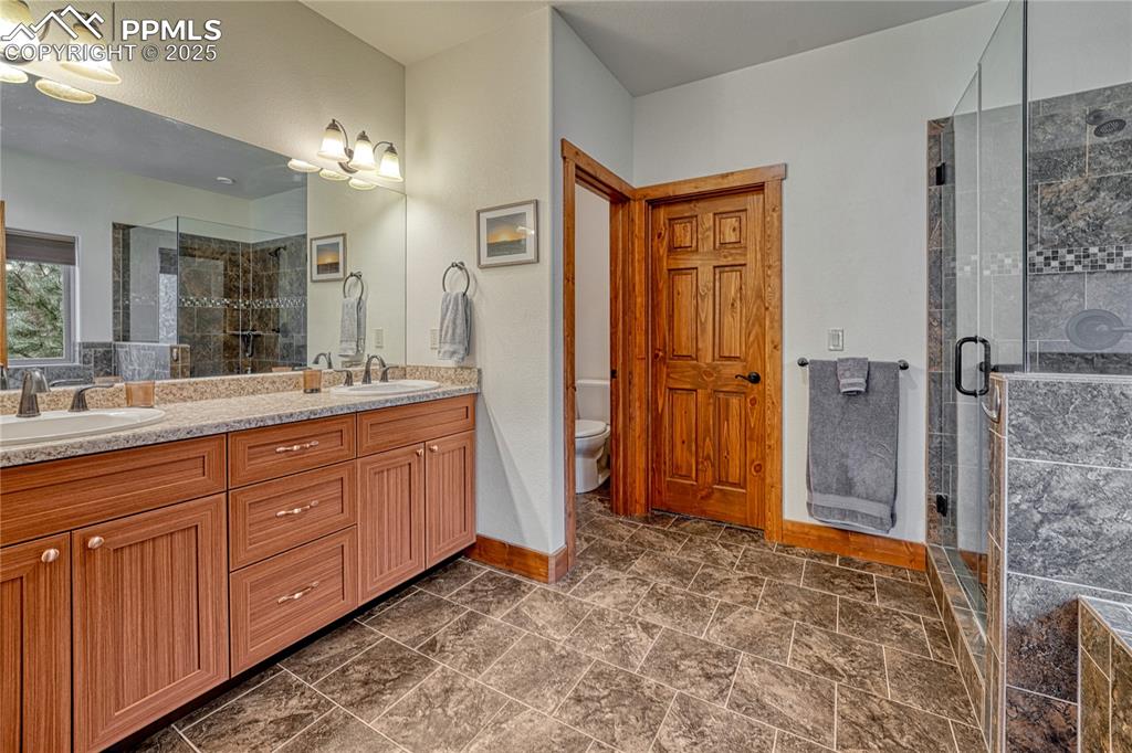 Bathroom with double vanity, a shower stall, baseboards, and toilet