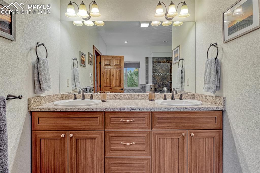 Bathroom with double vanity, a textured wall, tiled shower, and a chandelier