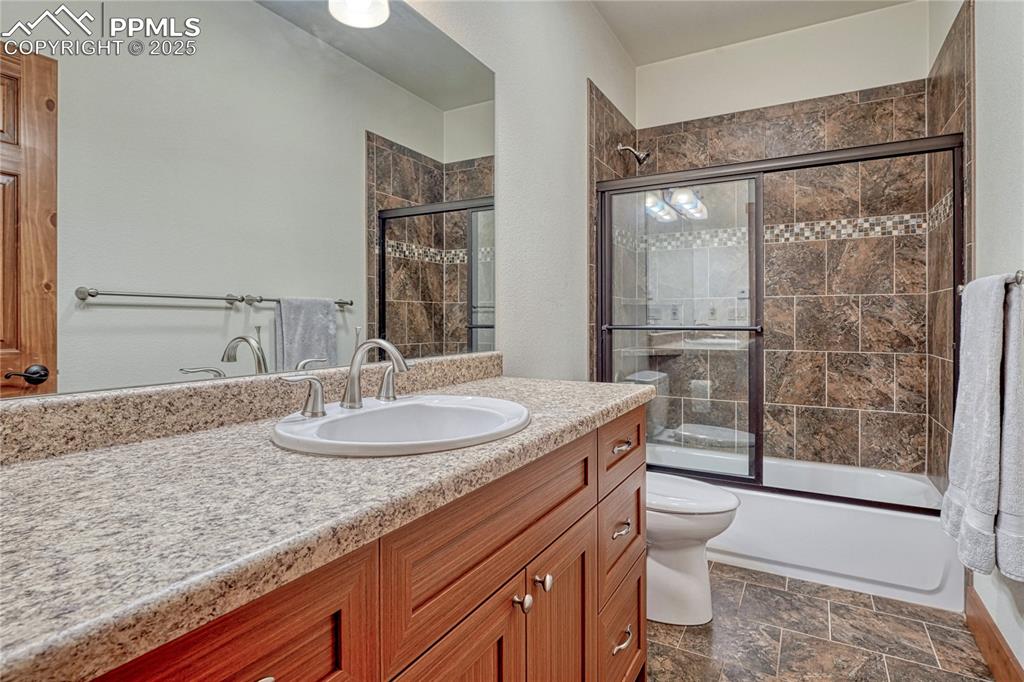Bathroom featuring toilet, vanity, combined bath / shower with glass door, and stone finish floors