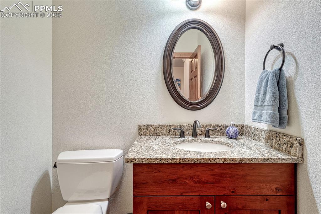 Half bathroom with vanity, toilet, and a textured wall