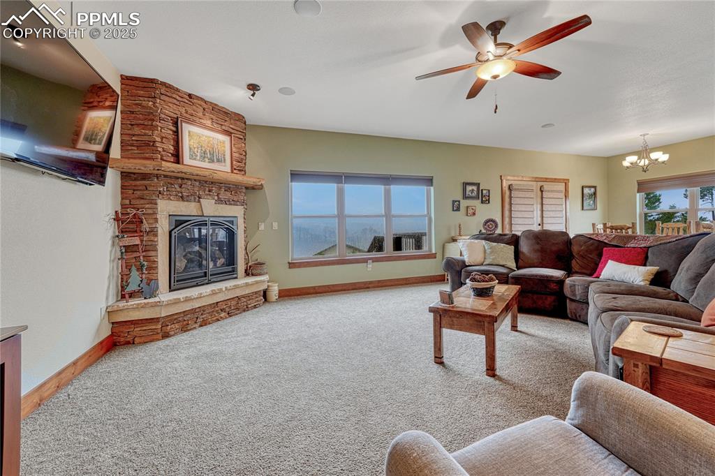 Living room featuring a stone fireplace, a chandelier, baseboards, and carpet flooring