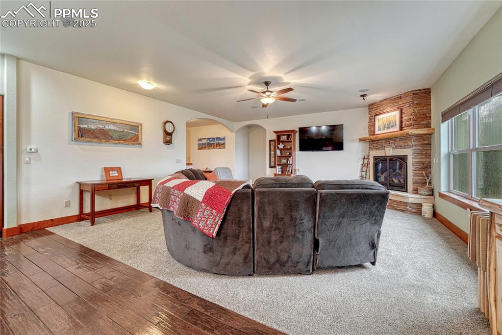 Living room featuring arched walkways, a ceiling fan, baseboards, a stone fireplace, and wood finished floors