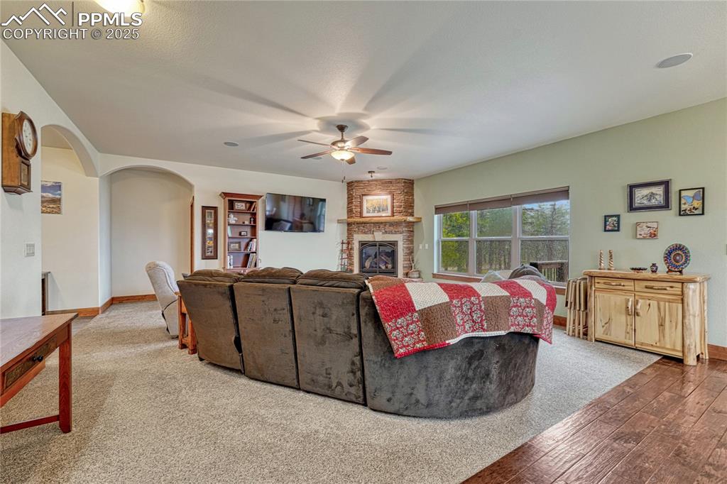 Living area with ceiling fan, arched walkways, a fireplace, hardwood / wood-style floors, and baseboards