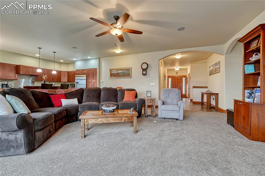 Living area featuring arched walkways, a ceiling fan, and light colored carpet