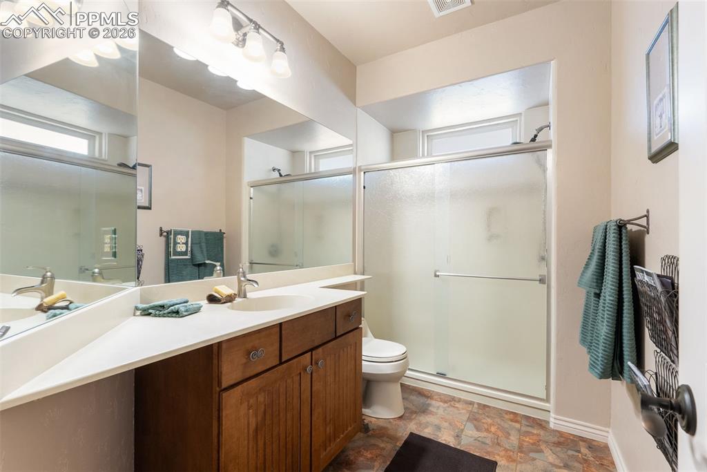 Full bath featuring vanity, a stall shower, and stone finish flooring