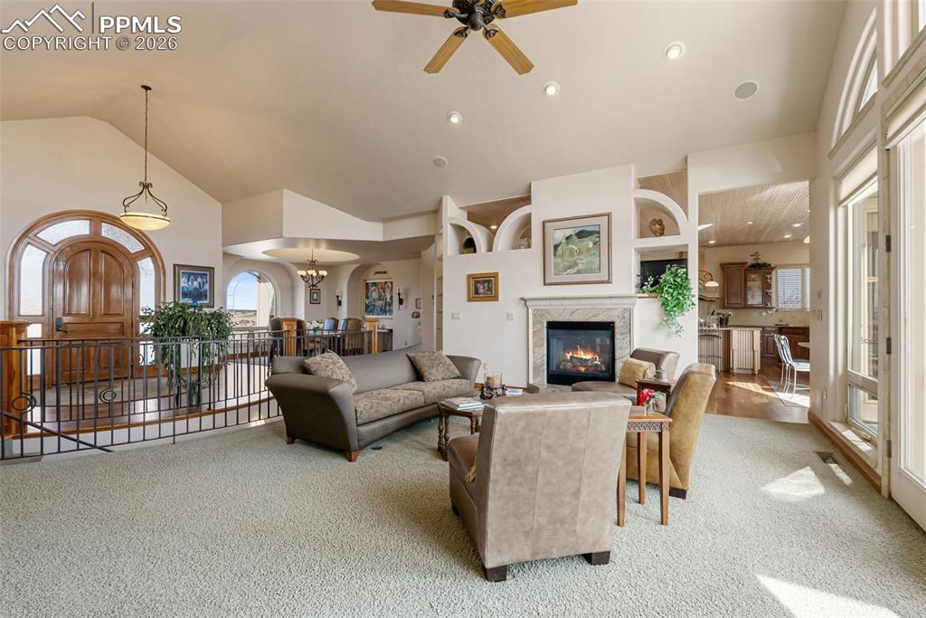 Carpeted living area with ceiling fan, lofted ceiling, a high end fireplace, and a chandelier