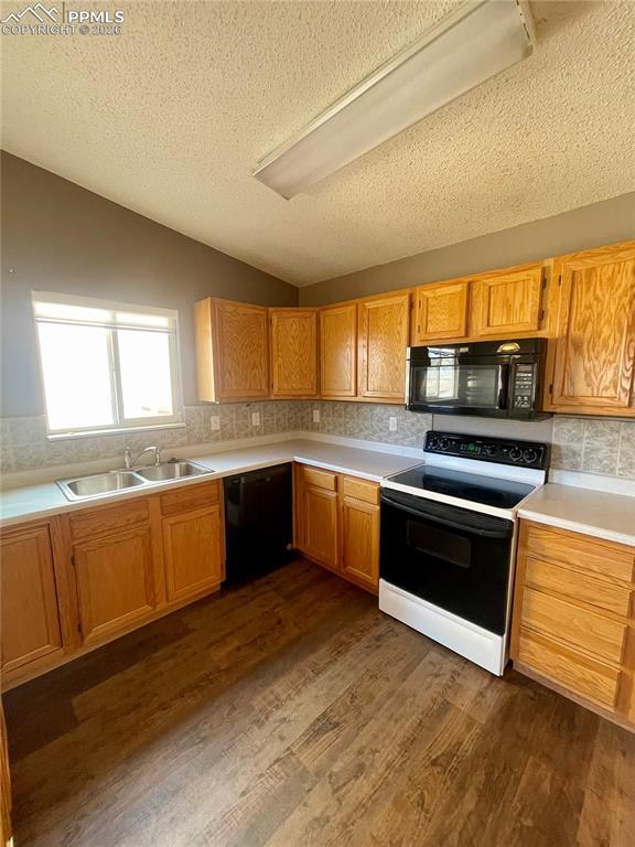 Kitchen with black appliances, light countertops, backsplash, and dark wood-style flooring