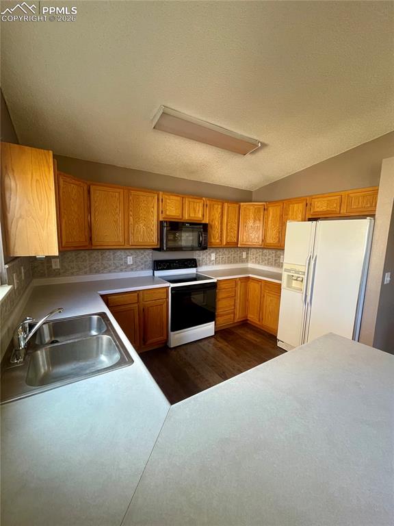 Kitchen with range with electric cooktop, white fridge with ice dispenser, light countertops, dark wood-type flooring, and wood finish cabinetry