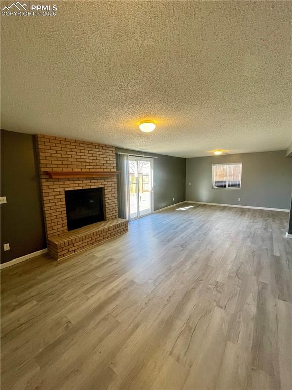 Unfurnished living room featuring a brick fireplace, a textured ceiling, and light wood-type flooring