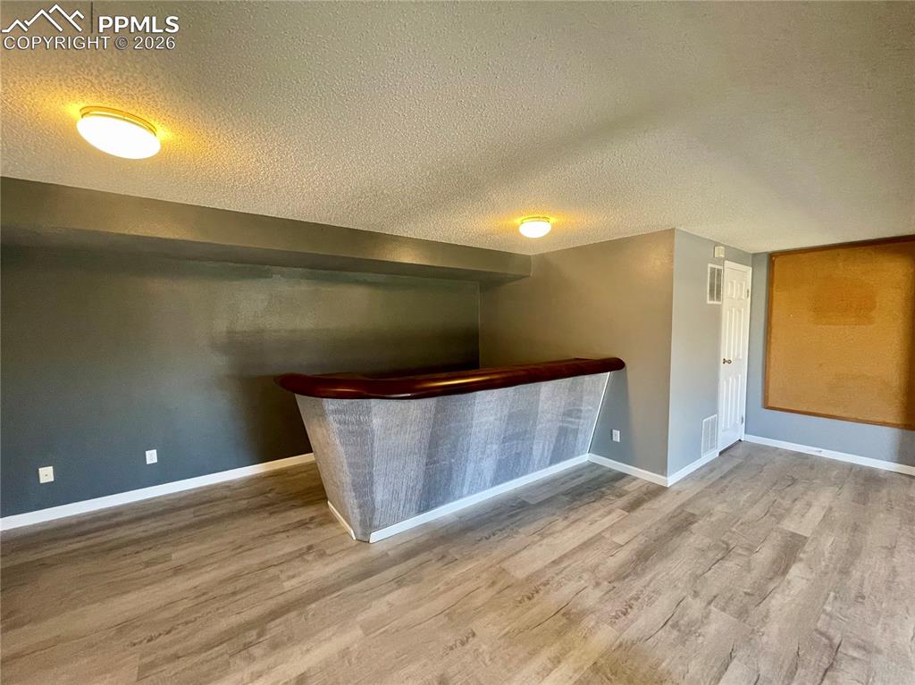 Indoor dry bar with a textured ceiling, light wood-type flooring, and dark countertops