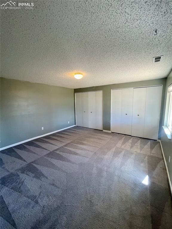 Unfurnished bedroom with a textured ceiling, carpet, and multiple closets