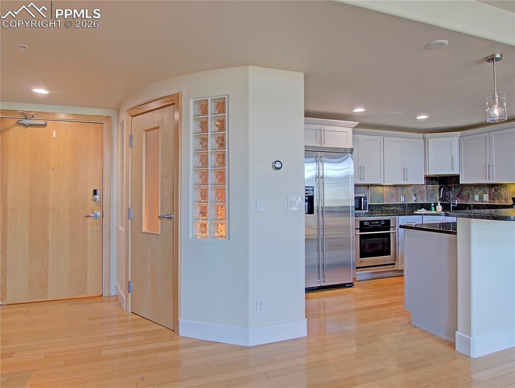 Kitchen featuring stainless steel appliances, white cabinets, light wood finished floors, and dark stone countertops
