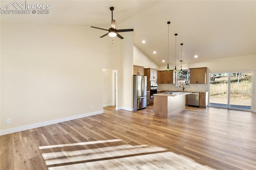 Kitchen with open floor plan, hanging light fixtures, a center island, high vaulted ceiling, and decorative backsplash