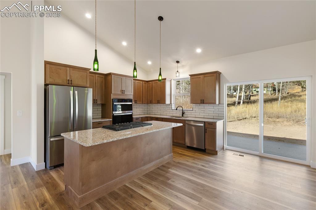 Kitchen with decorative backsplash, appliances with stainless steel finishes, light stone countertops, brown cabinetry, and recessed lighting
