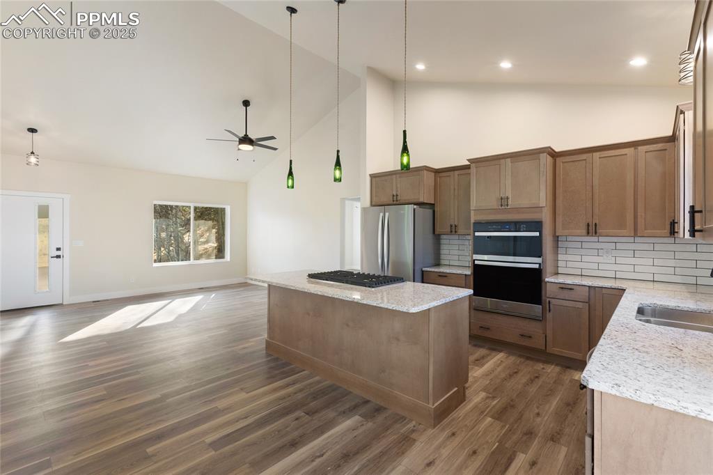 Kitchen with high vaulted ceiling, open floor plan, tasteful backsplash, a kitchen island, and light stone countertops
