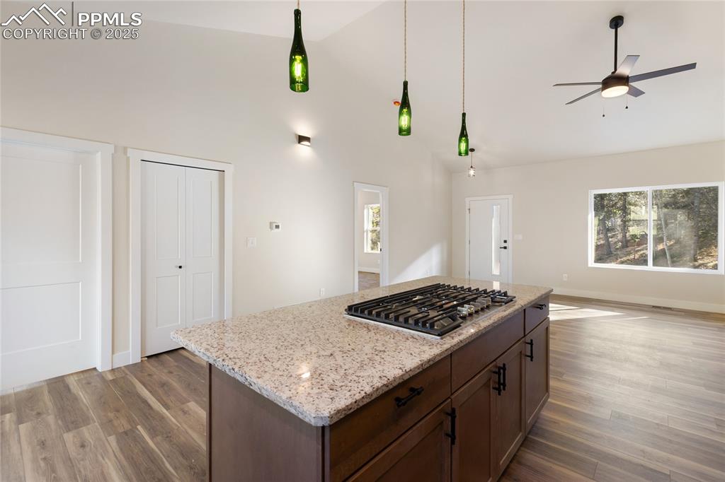 Kitchen with dark wood finished floors, ceiling fan, light stone countertops, stainless steel gas cooktop, and a kitchen island