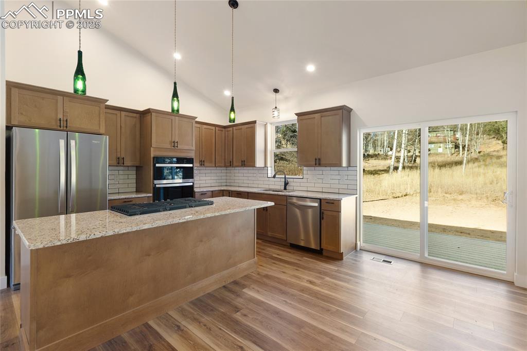 Kitchen featuring backsplash, a kitchen island, light stone countertops, brown cabinets, and decorative light fixtures