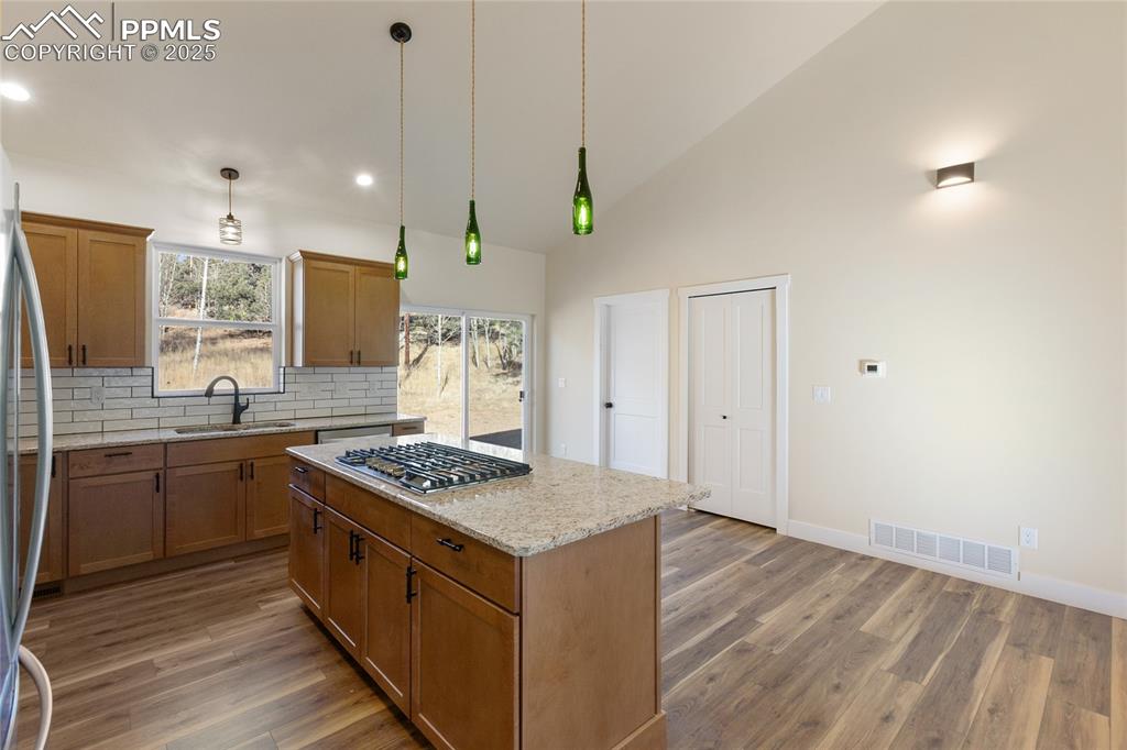 Kitchen with brown cabinetry, light stone countertops, decorative backsplash, a kitchen island, and pendant lighting