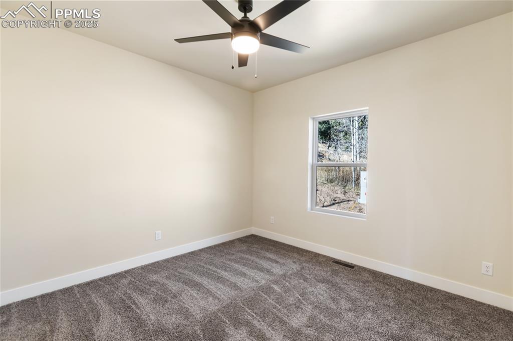 Empty room featuring dark carpet and a ceiling fan