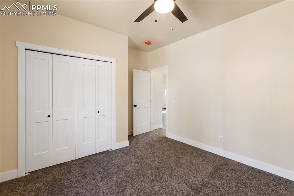 Unfurnished bedroom with dark colored carpet, a closet, and a ceiling fan