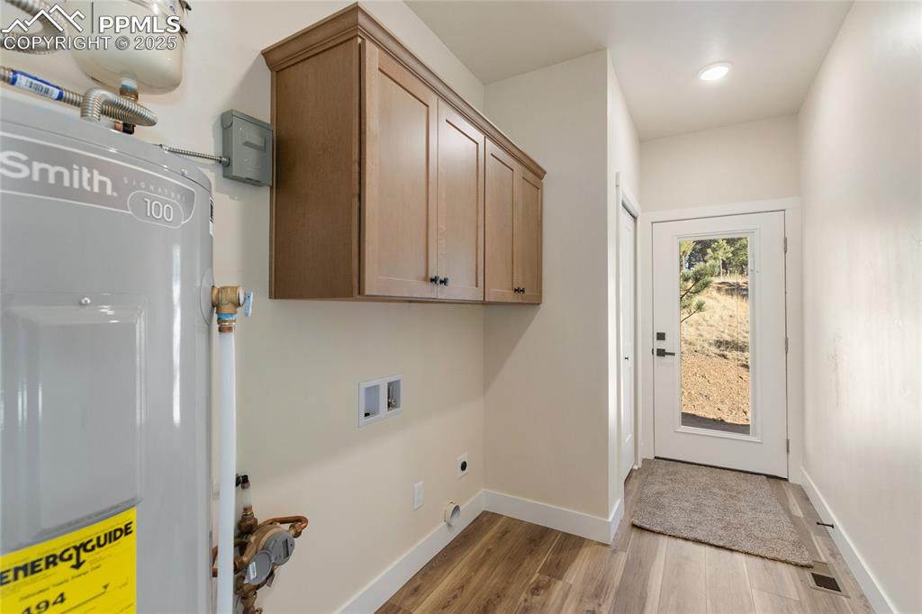 Laundry room featuring electric water heater, cabinet space, light wood-type flooring, washer hookup, and electric dryer hookup