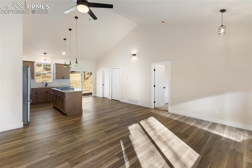 Unfurnished living room featuring high vaulted ceiling, dark wood-type flooring, and ceiling fan