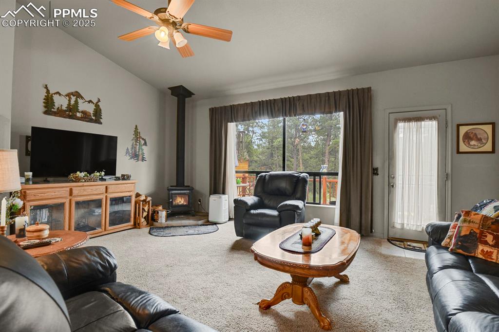 Carpeted living area featuring plenty of natural light, a wood stove, a ceiling fan, and lofted ceiling