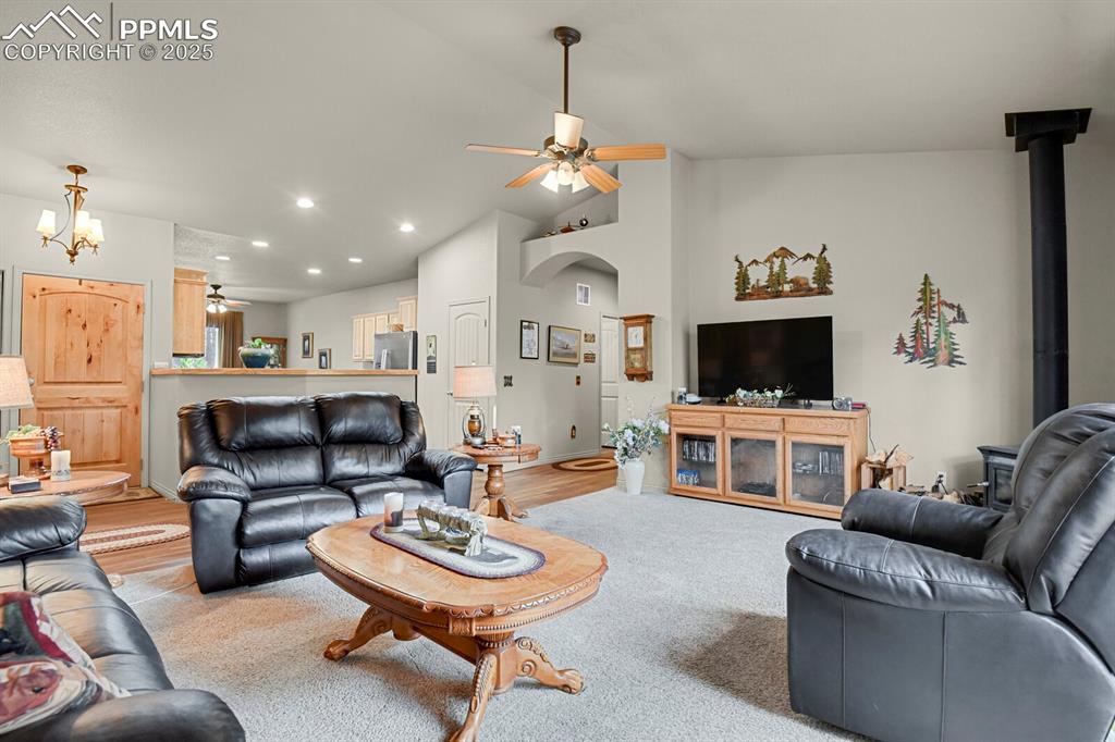 Living room featuring ceiling fan, vaulted ceiling, arched walkways, recessed lighting, and a wood stove