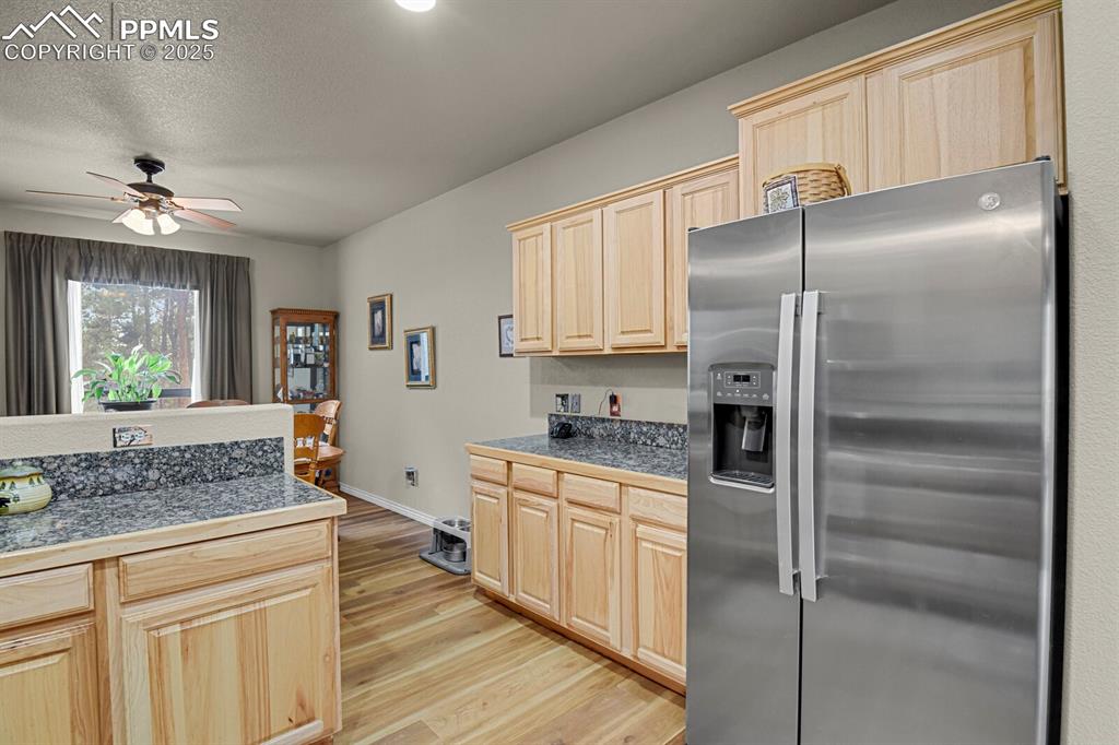 Kitchen featuring tile countertops, stainless steel refrigerator with ice dispenser, light brown cabinetry, light wood-style floors, and ceiling fan