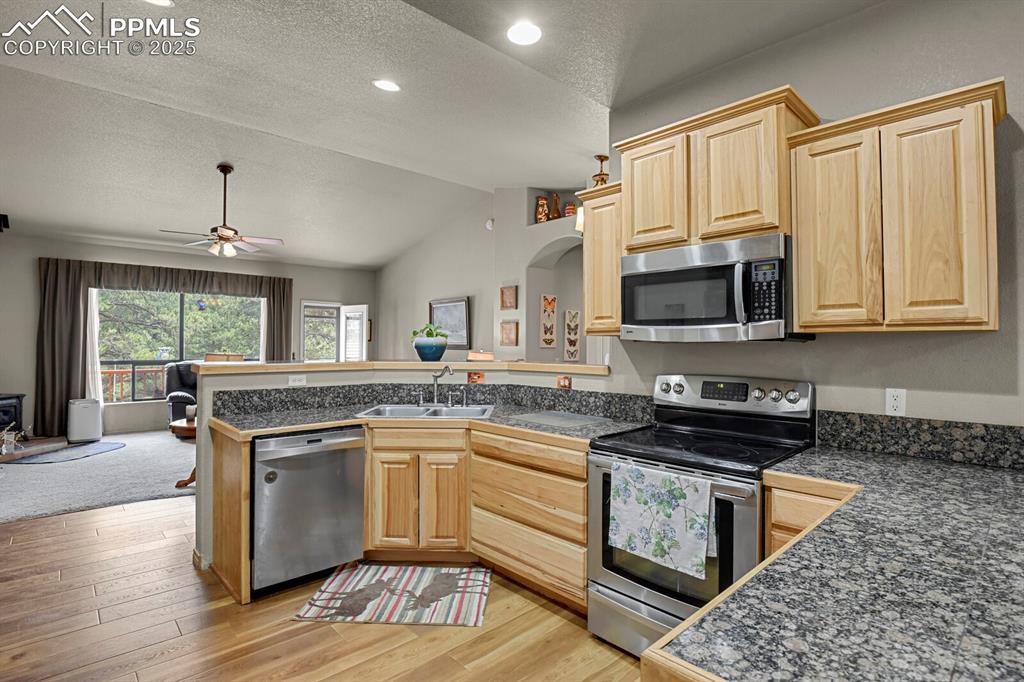 Kitchen featuring stainless steel appliances, a peninsula, light brown cabinets, lofted ceiling, and tile counters