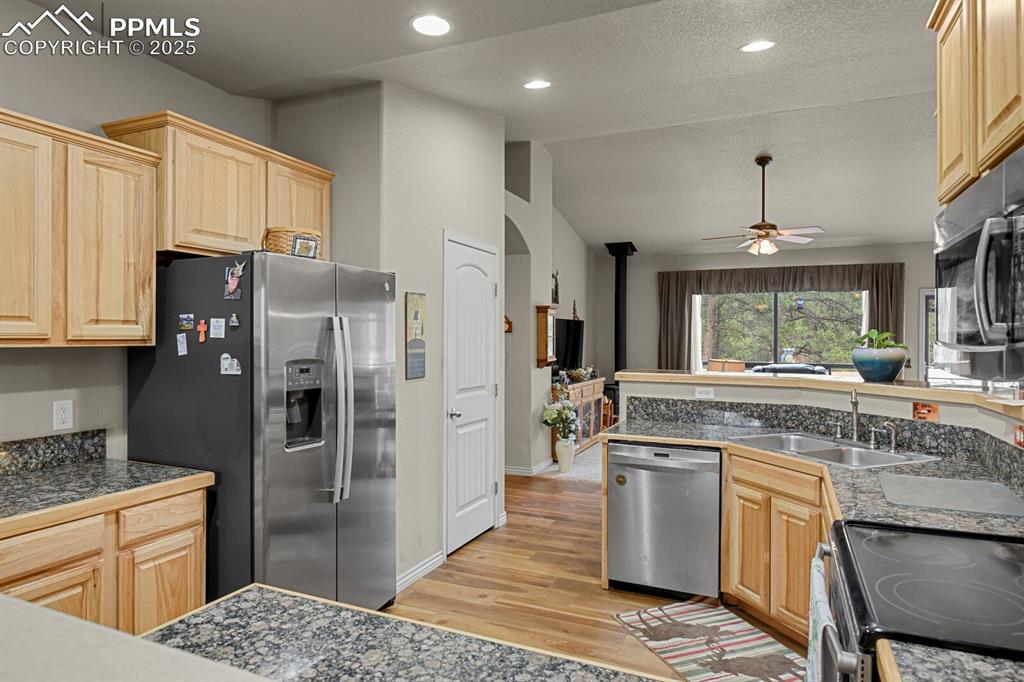 Kitchen featuring tile counters, stainless steel appliances, light brown cabinets, vaulted ceiling, and light wood-style floors