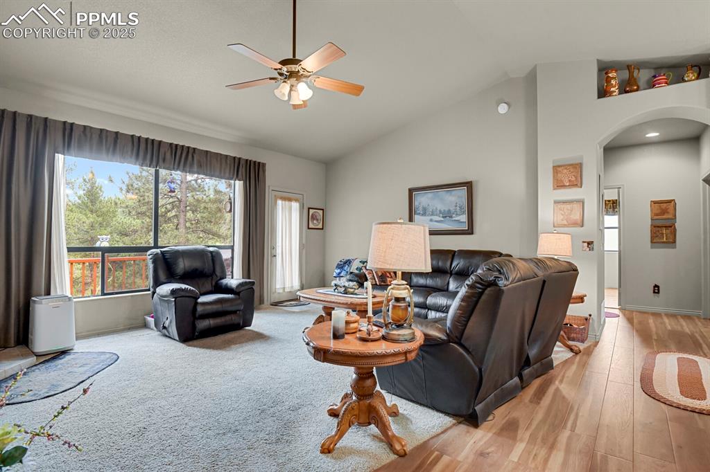 Living area with arched walkways, lofted ceiling, a ceiling fan, and light wood-style floors