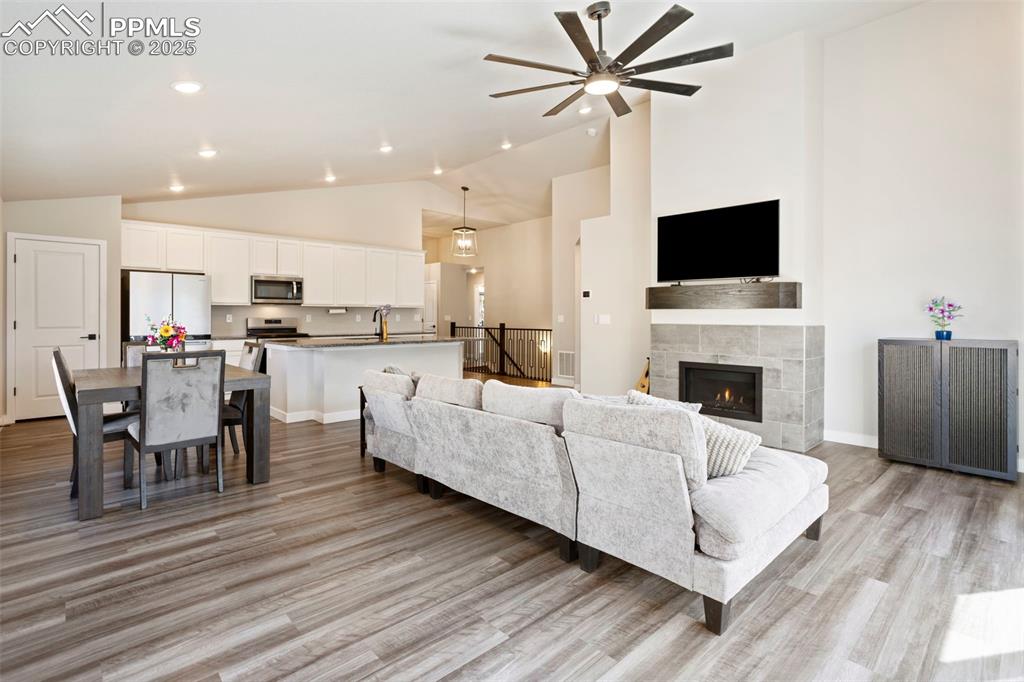 Living area with high vaulted ceiling, light wood finished floors, a tiled fireplace, a ceiling fan, and recessed lighting