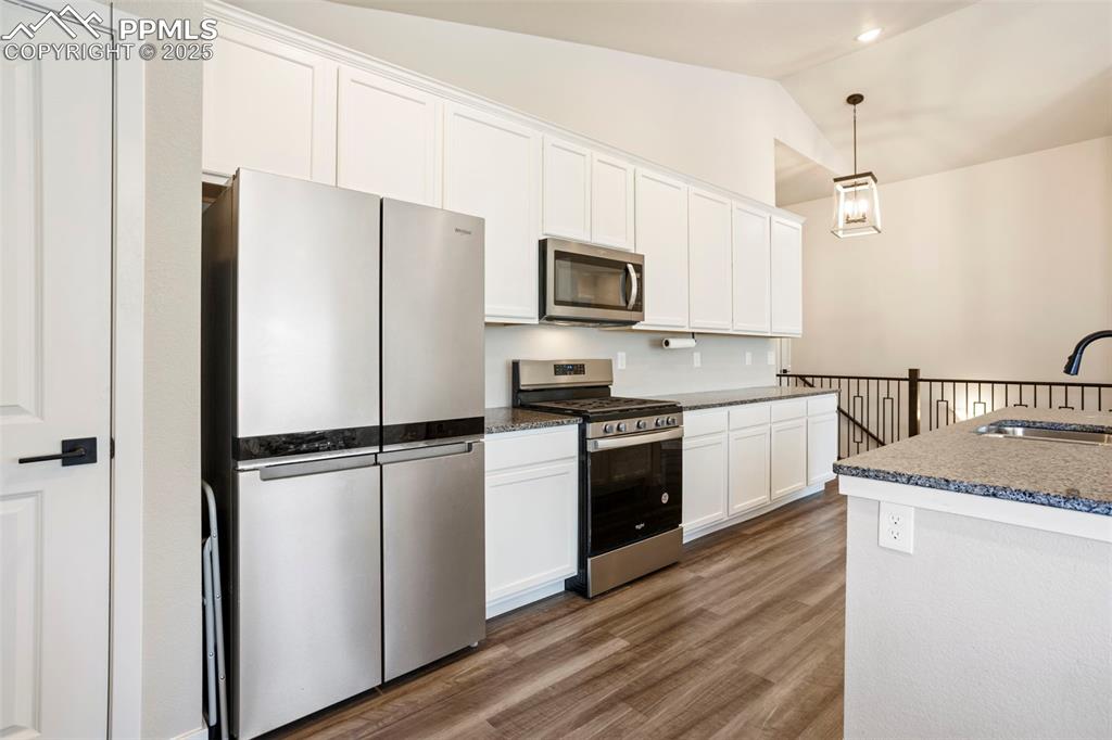Kitchen featuring appliances with stainless steel finishes, white cabinetry, dark wood-style flooring, lofted ceiling, and hanging light fixtures
