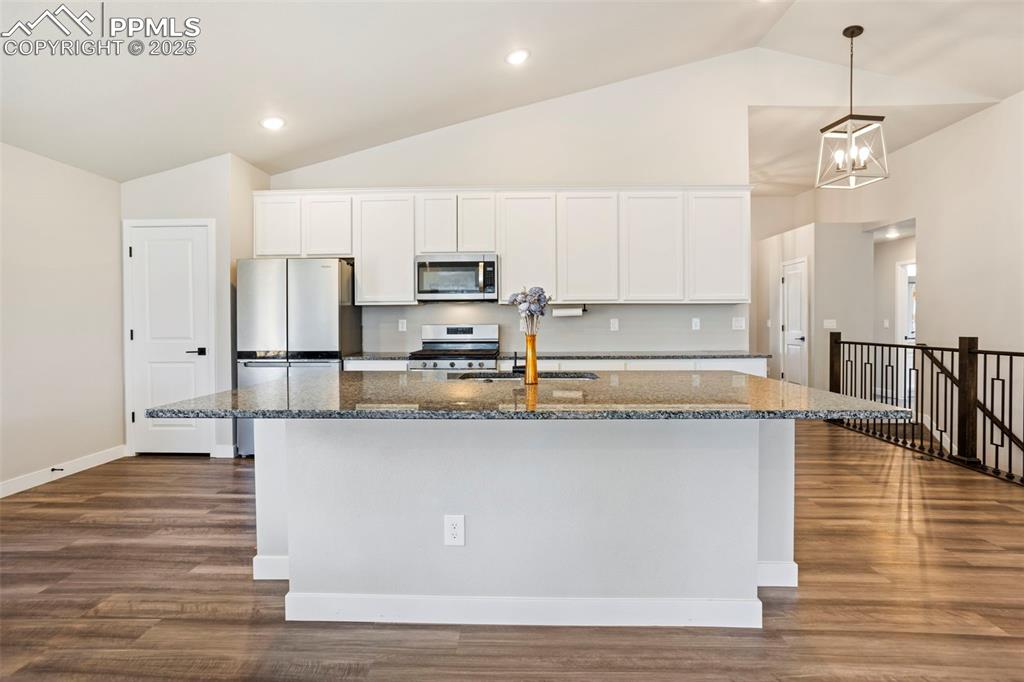Kitchen featuring white cabinetry, dark stone counters, appliances with stainless steel finishes, a center island with sink, and vaulted ceiling