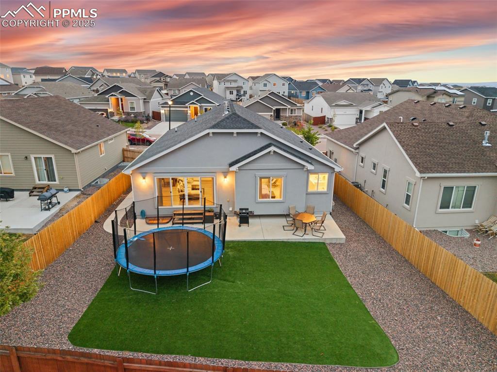 Rear view of property featuring a patio, stucco siding, a trampoline, a fenced backyard, and a residential view