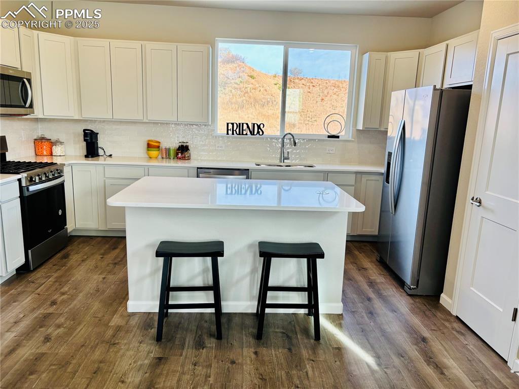 Kitchen featuring stainless steel appliances, tasteful backsplash, white cabinetry, a kitchen island, and a kitchen bar
