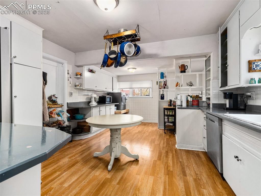 Kitchen featuring open shelves, white cabinets, dark countertops, light wood-style floors, and stainless steel appliances